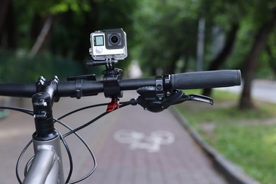 Photo of Modern action camera with mount on bicycle outdoors, closeup