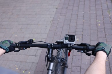 Photo of Man riding bicycle with modern action camera outdoors, closeup