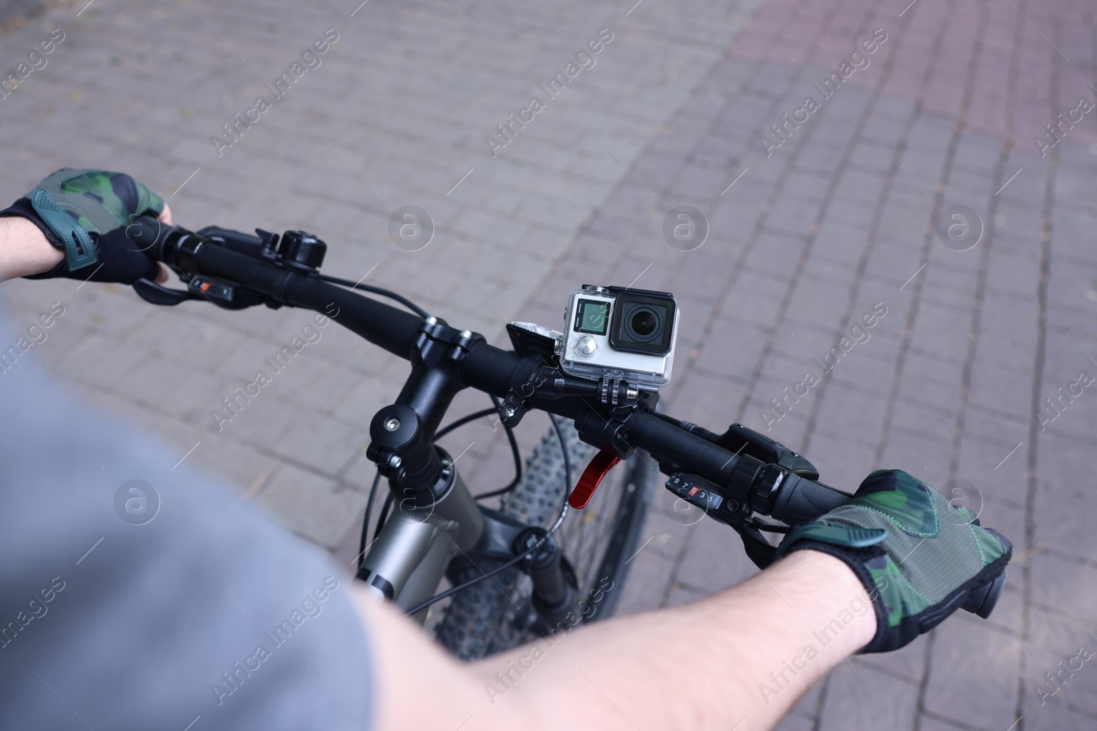 Photo of Man riding bicycle with modern action camera outdoors, closeup