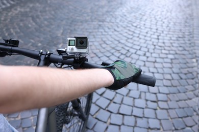 Photo of Man riding bicycle with modern action camera outdoors, closeup