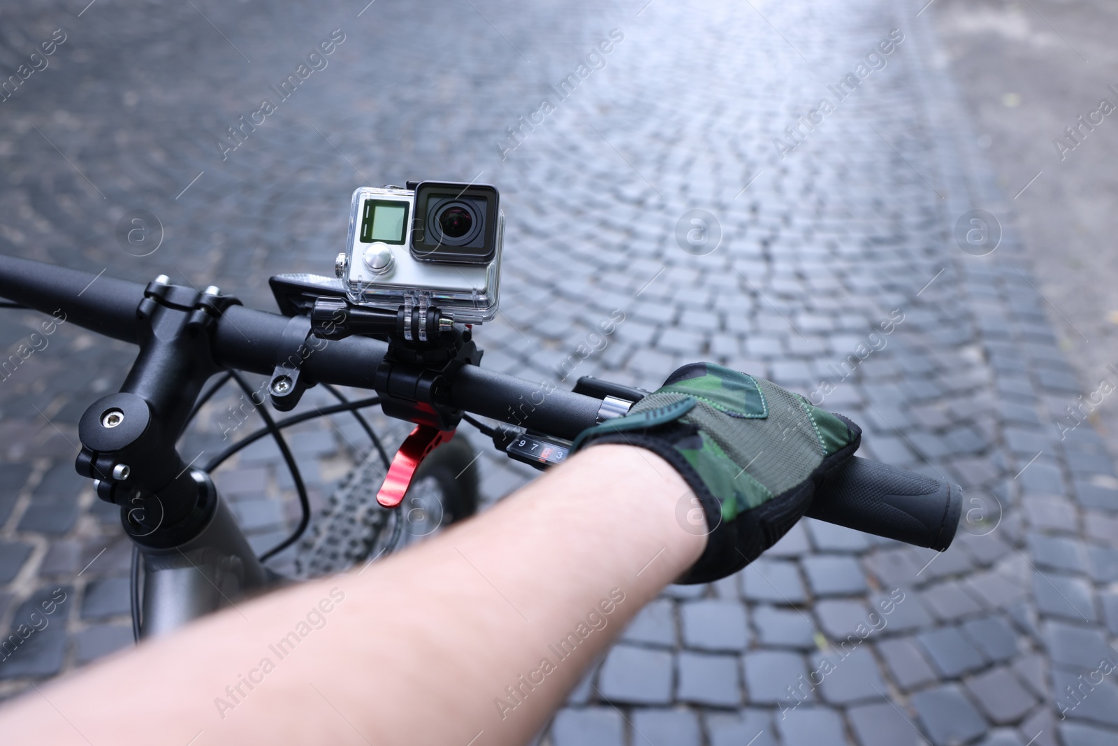 Photo of Man riding bicycle with modern action camera outdoors, closeup