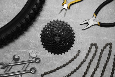 Photo of Wrenches, pliers, bicycle tire, cassette and chain on grey textured background, flat lay