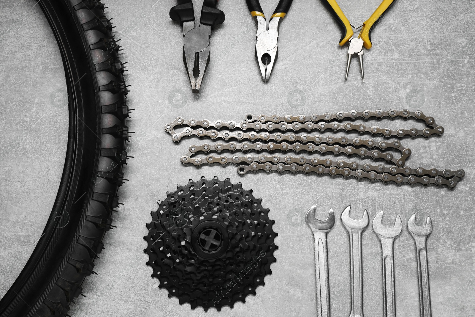 Photo of Wrenches, pliers, bicycle tire, cassette and chain on grey textured background, flat lay