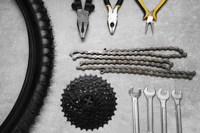 Wrenches, pliers, bicycle tire, cassette and chain on grey textured background, flat lay