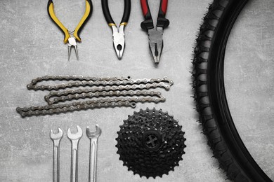 Wrenches, pliers, bicycle tire, cassette and chain on grey textured background, flat lay