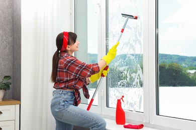 Photo of Young woman with squeegee tool cleaning window indoors