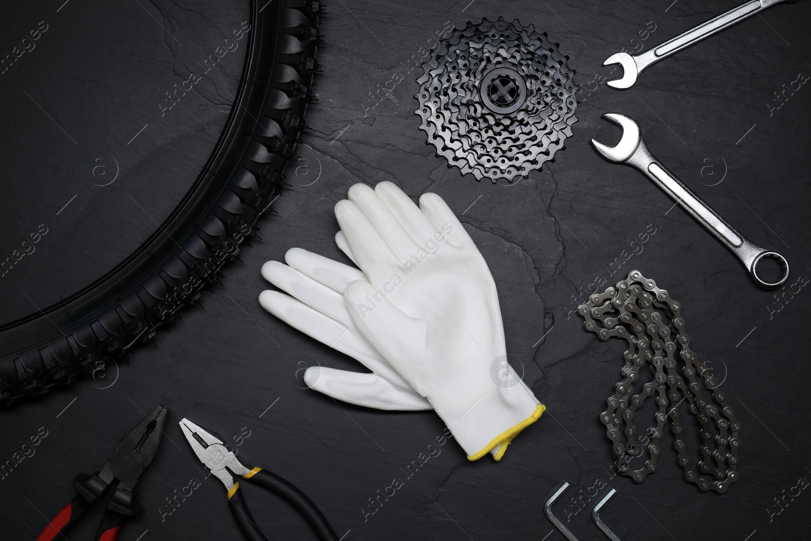 Photo of Flat lay composition with different bicycle components, tools and gloves on dark gray textured background