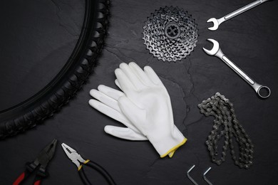 Flat lay composition with different bicycle components, tools and gloves on dark gray textured background