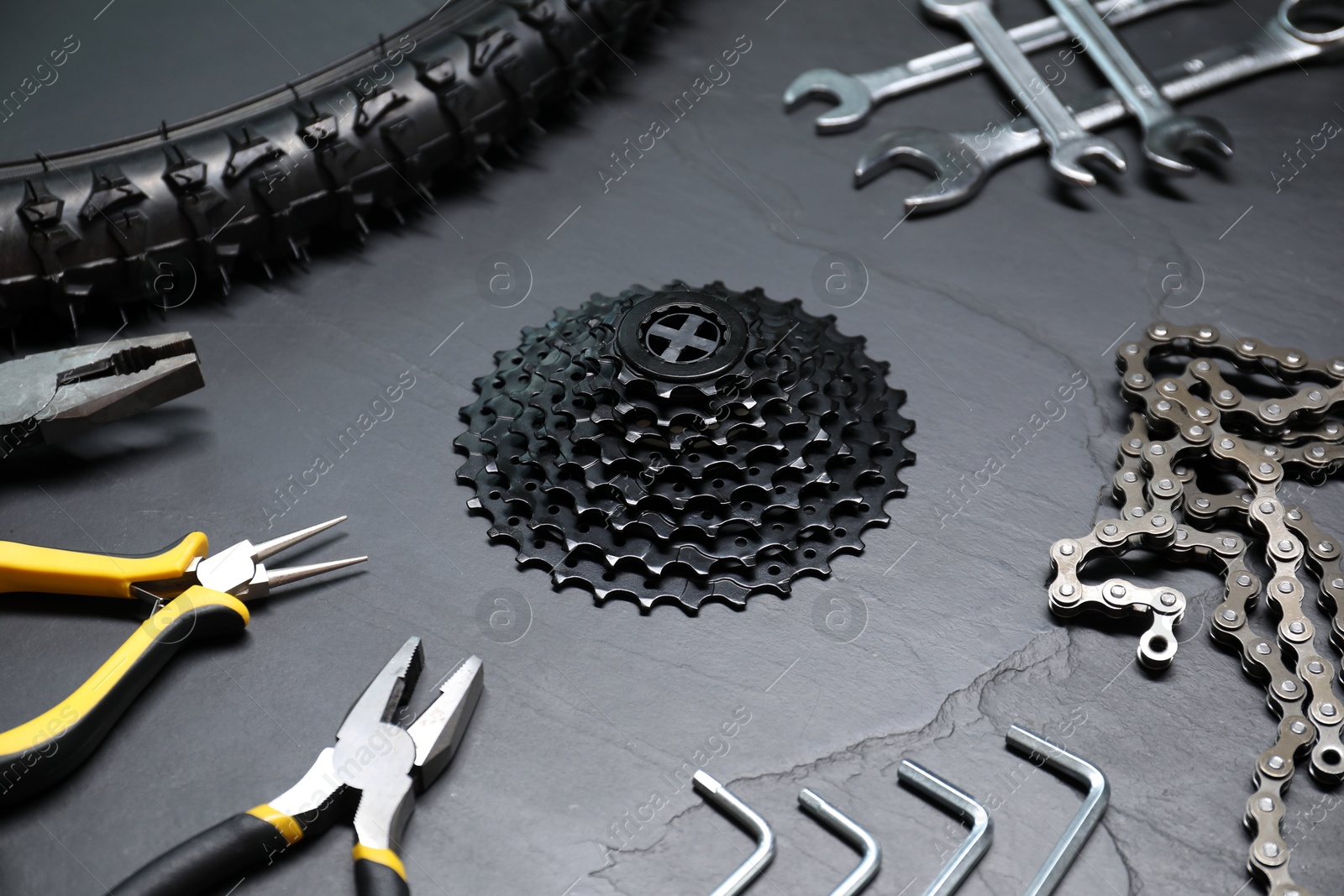 Photo of Wrenches, pliers, bicycle tire, cassette and chain on dark gray textured background, closeup