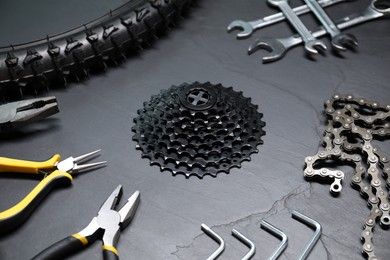 Photo of Wrenches, pliers, bicycle tire, cassette and chain on dark gray textured background, closeup