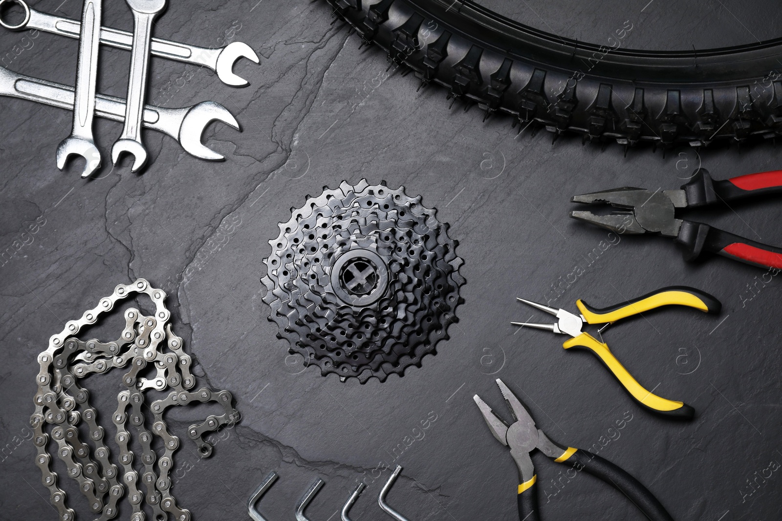 Photo of Wrenches, pliers, bicycle tire, cassette and chain on dark gray textured background, flat lay