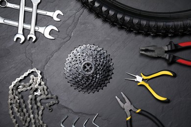 Wrenches, pliers, bicycle tire, cassette and chain on dark gray textured background, flat lay