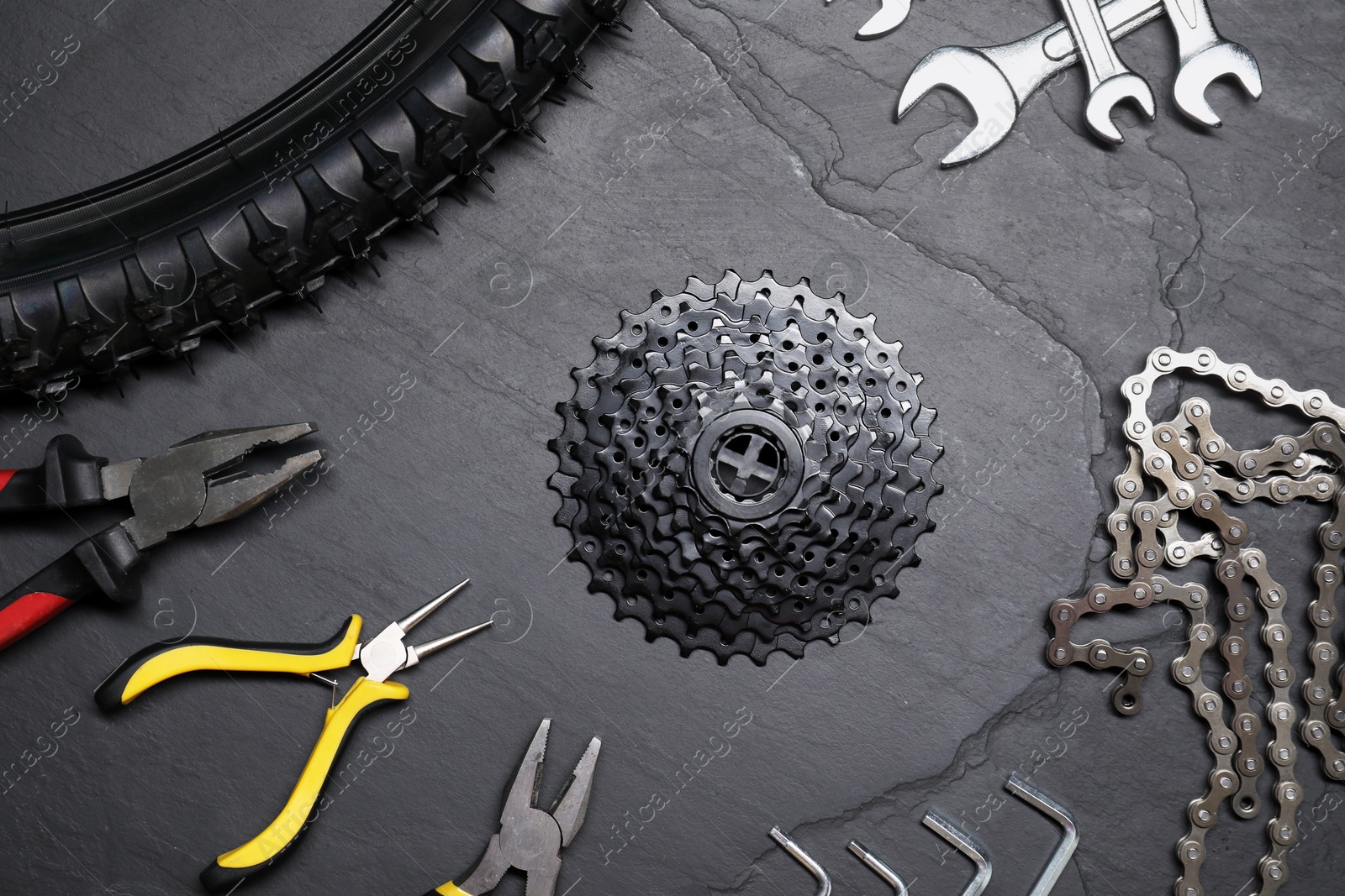 Photo of Wrenches, pliers, bicycle tire, cassette and chain on dark gray textured background, flat lay