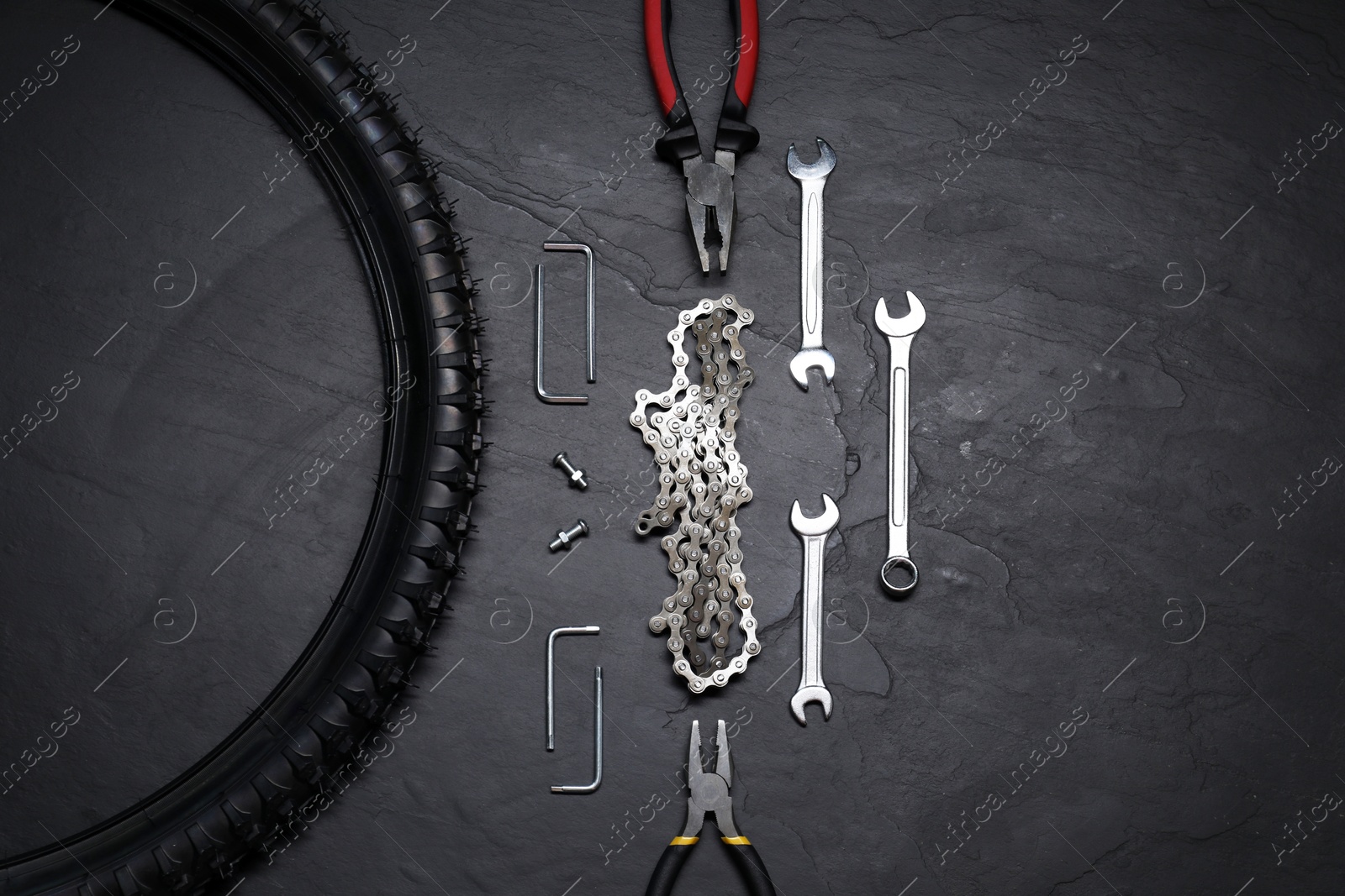 Photo of Wrenches, pliers, bicycle tire and chain on dark gray textured background, flat lay