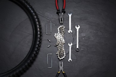 Wrenches, pliers, bicycle tire and chain on dark gray textured background, flat lay