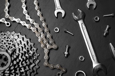 Different bicycle components and tools on dark gray textured background, flat lay