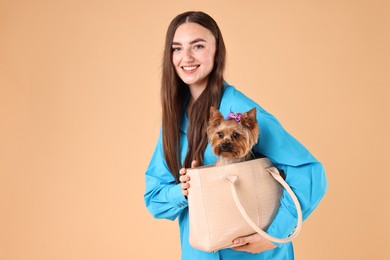 Beautiful young woman carrying cute Yorkshire Terrier dog in bag on beige background