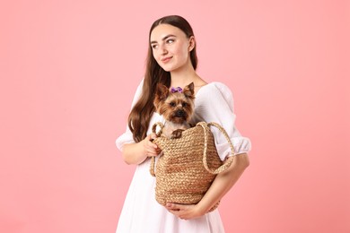 Photo of Beautiful young woman holding wicker bag with cute Yorkshire Terrier dog on pink background