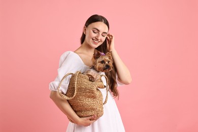 Photo of Beautiful young woman holding wicker bag with cute Yorkshire Terrier dog on pink background