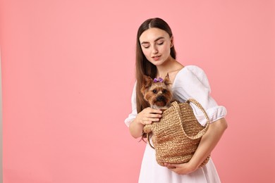 Photo of Beautiful young woman holding wicker bag with cute Yorkshire Terrier dog on pink background, space for text