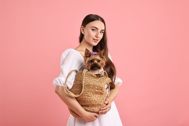 Photo of Beautiful young woman holding wicker bag with cute Yorkshire Terrier dog on pink background