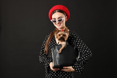 Woman in sunglasses holding bag with cute Yorkshire Terrier dog on black background