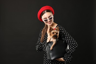 Photo of Woman in sunglasses holding bag with cute Yorkshire Terrier dog on black background