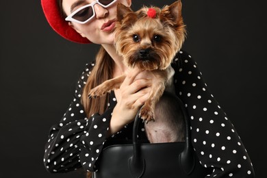 Woman in sunglasses holding bag with cute Yorkshire Terrier dog on black background, selective focus