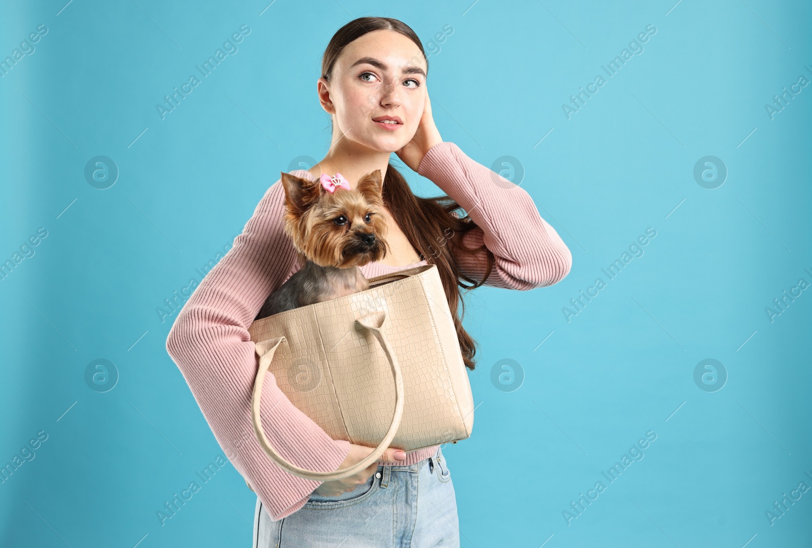 Photo of Beautiful young woman holding bag with cute Yorkshire Terrier dog on light blue background