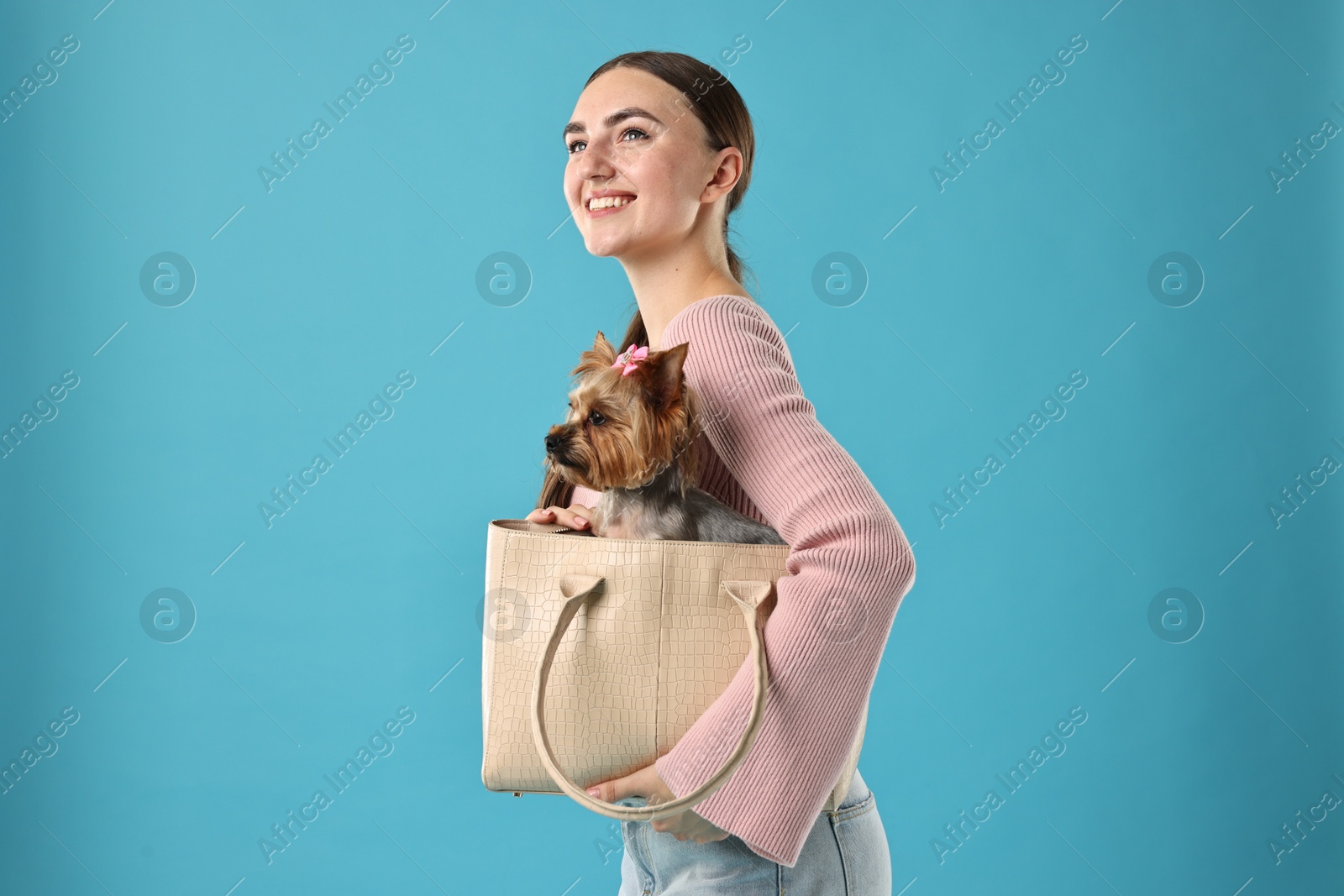 Photo of Beautiful young woman holding bag with cute Yorkshire Terrier dog on light blue background