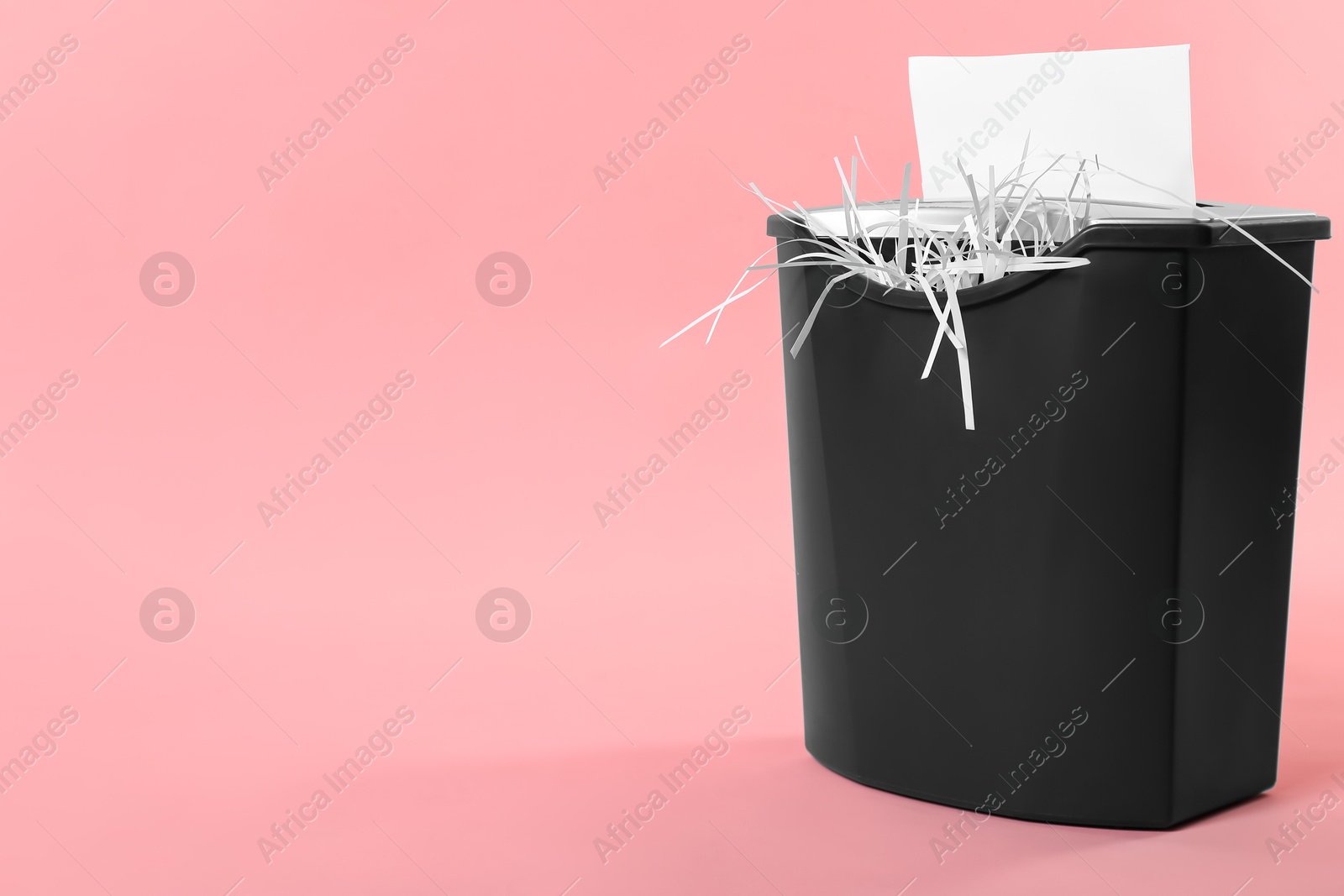 Photo of Destroying sheet of paper with shredder on pink background, space for text