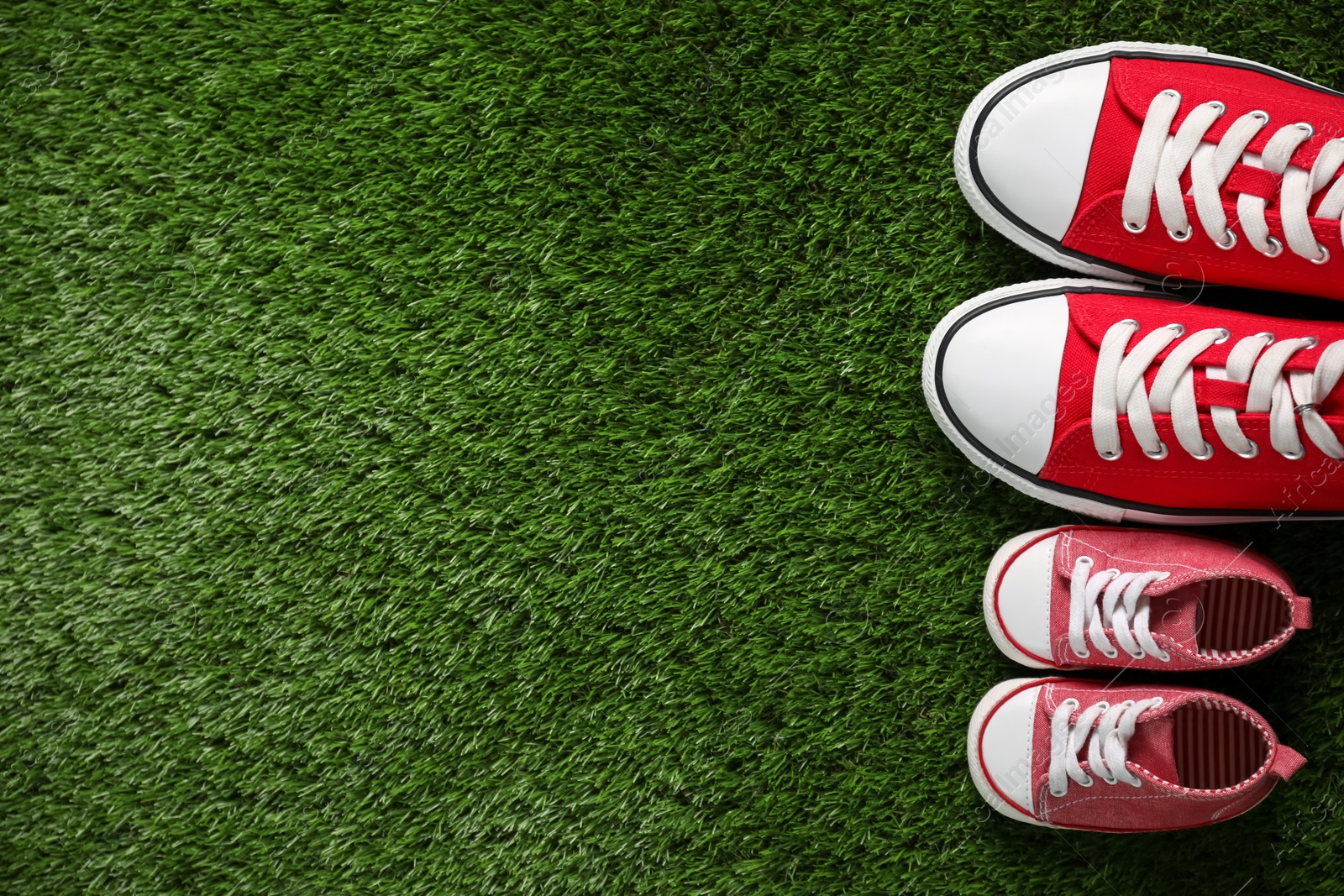 Photo of Big and small shoes on green grass, top view. Space for text