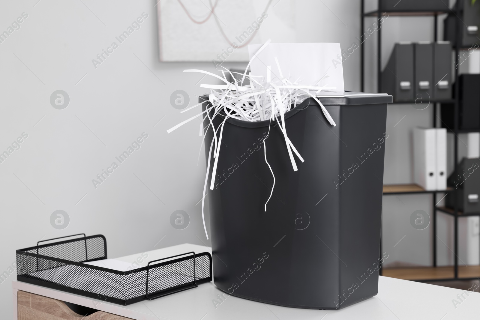 Photo of Destroying sheet of paper with shredder on white table in office