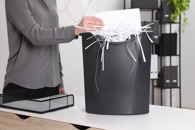 Photo of Woman destroying sheet of paper with shredder at white table in office, closeup