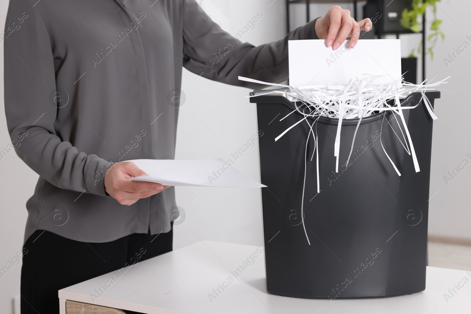 Photo of Woman destroying paper with shredder at white table in office, closeup