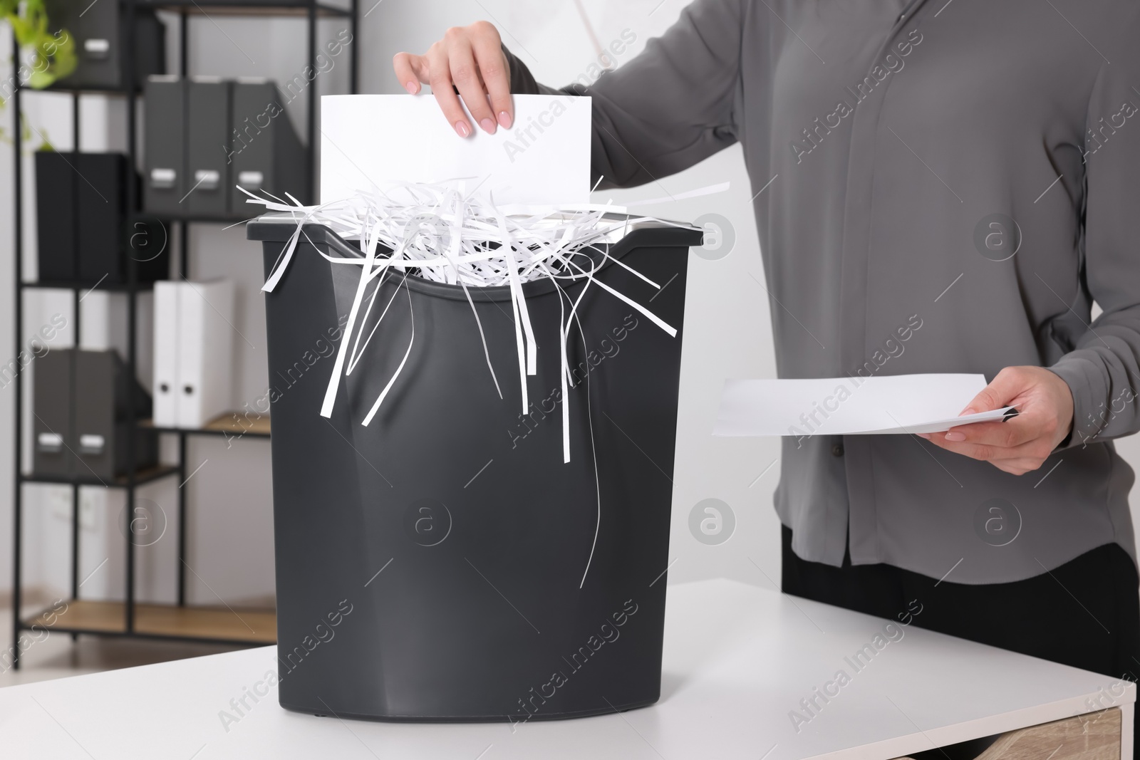 Photo of Woman destroying paper with shredder at white table in office, closeup