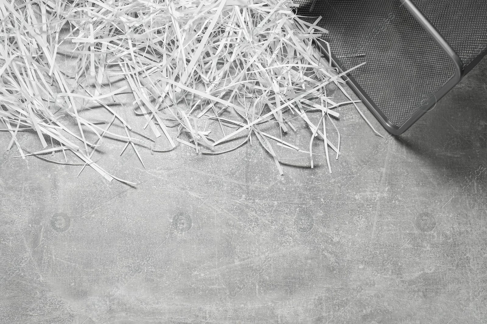 Photo of Shredded paper strips with trash bin on grey textured table, top view. Space for text