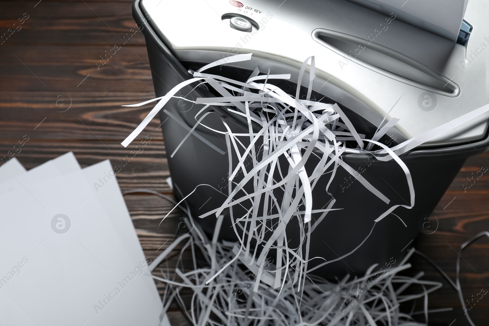 Photo of Shredder, black bin, paper strips and sheets on wooden table