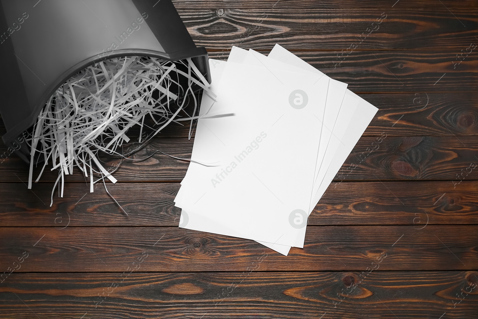 Photo of Black bin with paper strips and sheets on wooden table, flat lay