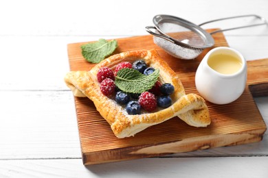 Tasty puff pastry with berries on white wooden table, space for text