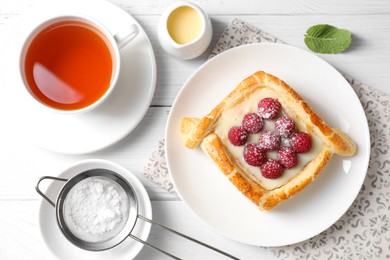 Photo of Tasty puff pastry with raspberries and tea on white wooden table, flat lay