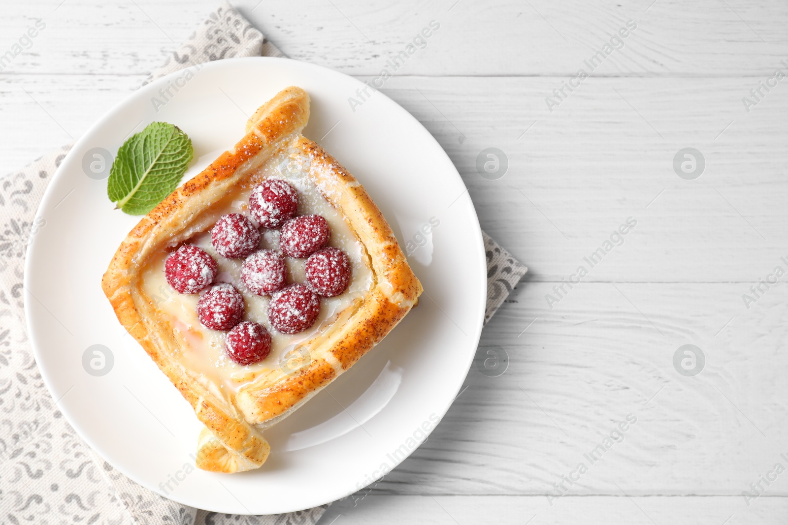 Photo of Tasty puff pastry with raspberries on white wooden table, top view. Space for text