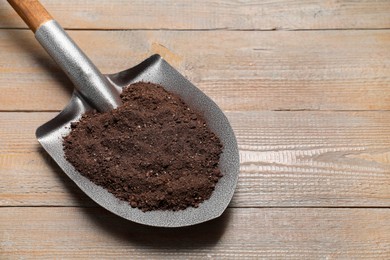 Photo of Metal shovel with soil on wooden table, space for text