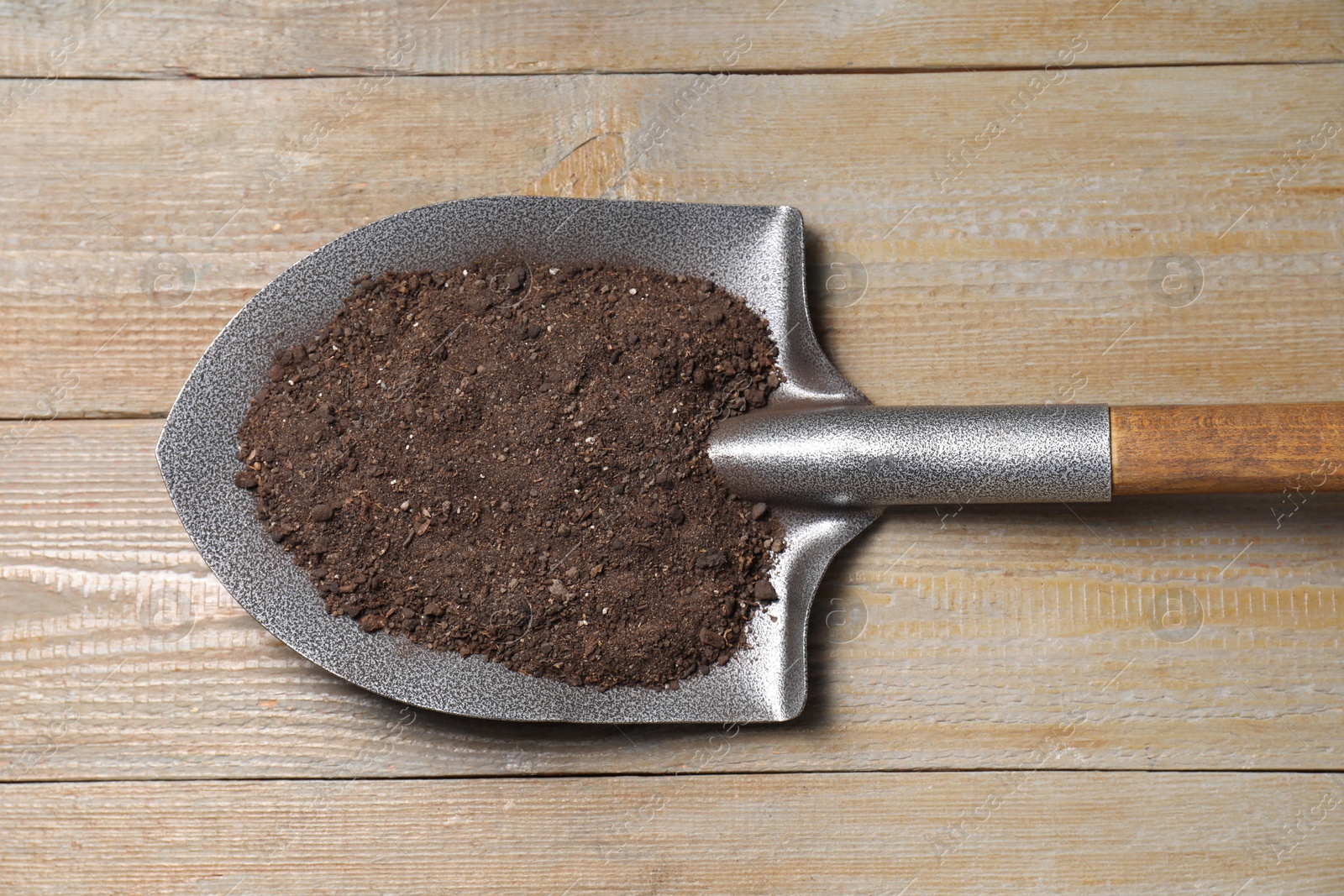 Photo of Metal shovel with soil on wooden table, top view