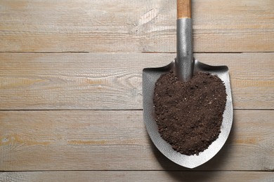 Photo of Metal shovel with soil on wooden table, top view. Space for text