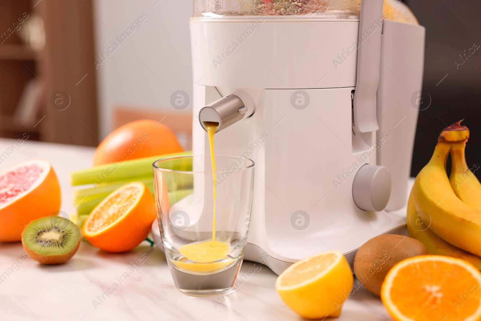 Photo of Modern juicer, fresh fruits and glass on white marble table in kitchen