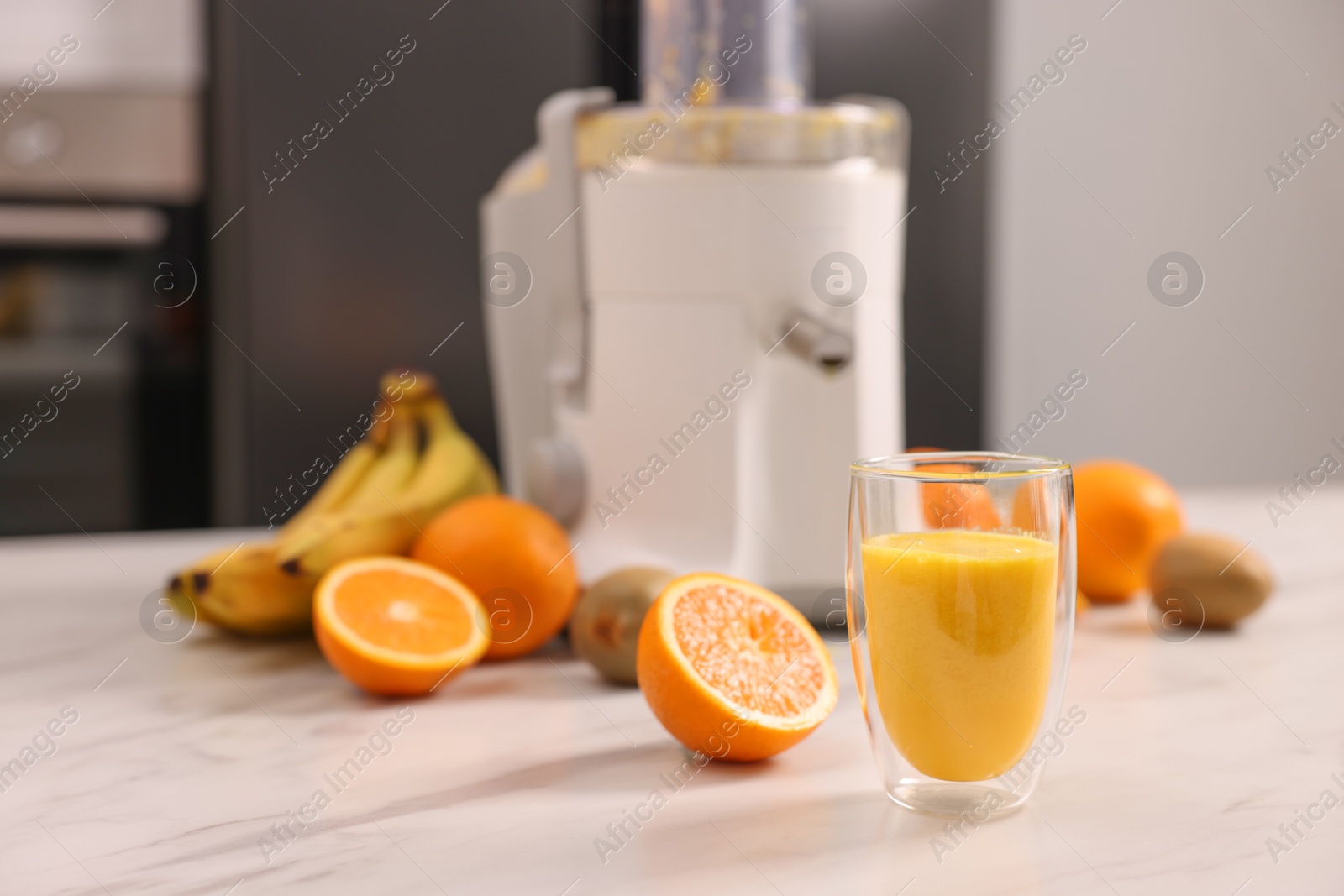 Photo of Modern juicer, fresh fruits and glass on white marble table in kitchen, selective focus