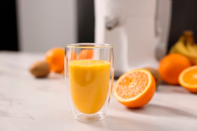 Photo of Glass of fresh juice, modern juicer and fruits on white marble table in kitchen, selective focus