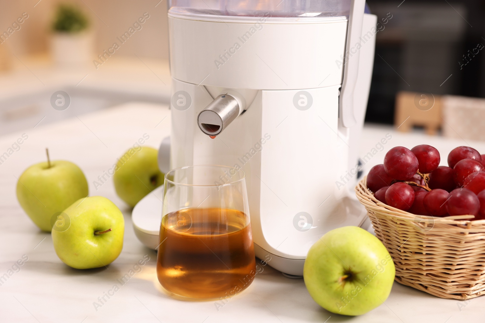 Photo of Modern juicer, fresh fruits and glass on white marble table in kitchen, closeup