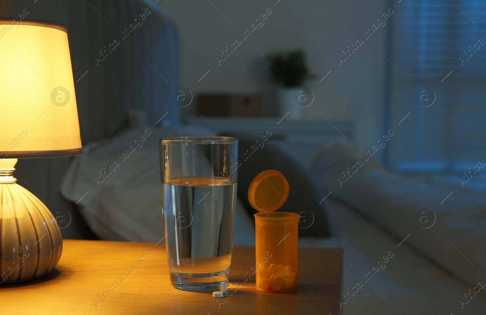 Photo of Insomnia treatment. Glass of water and pills on bedside table in bedroom at night